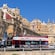 A bus with a sign on its side reading ‘hop on, malta sightseeing, hop off’ is parked near ancient buildings